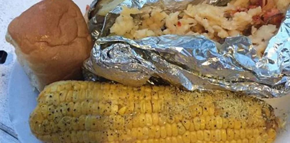 A plated dinner of foil-wrapped seafood, a dinner roll, and buttered corn on the cob at Bimini Big Game Club’s restaurant