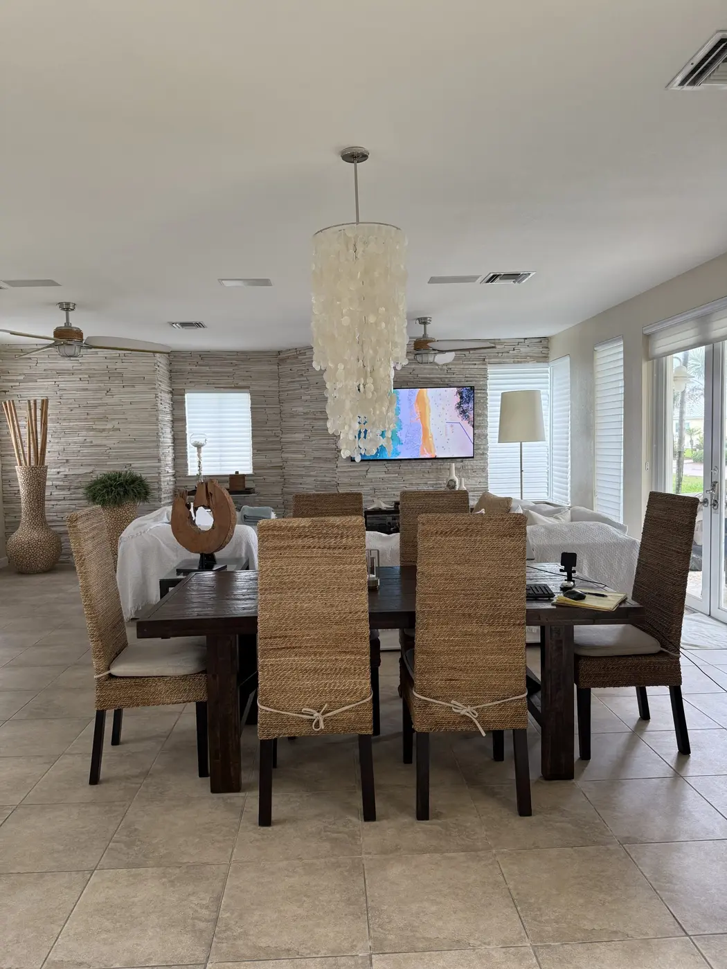 The open-plan dining and living area inside Bimini Paradise, with a woven dining set and a capiz-shell chandelier