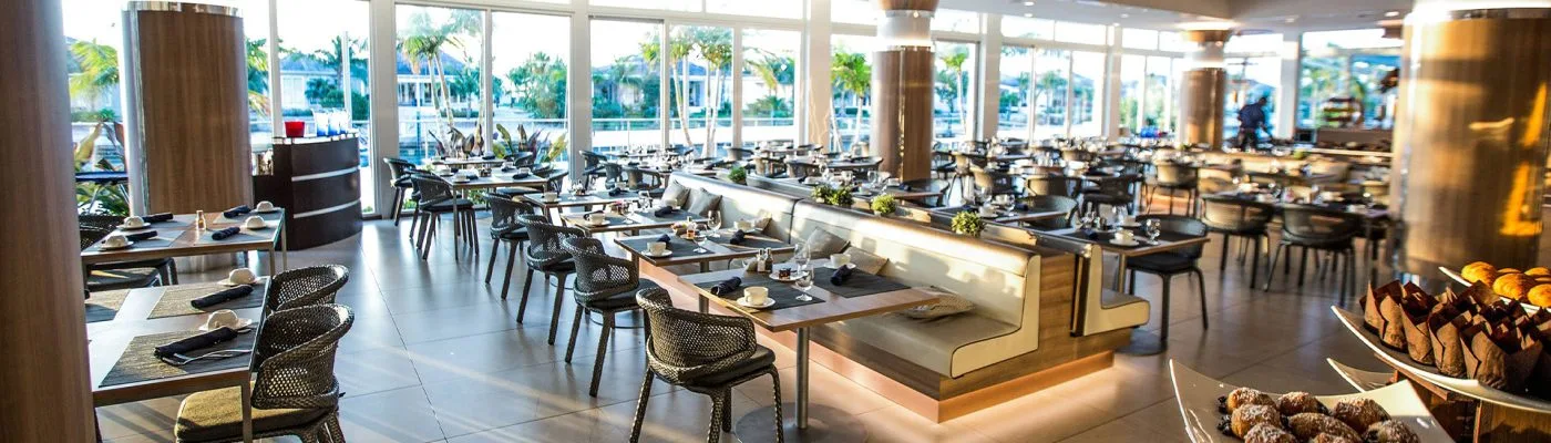 The Tides restaurant dining room at the Hilton at Resorts World Bimini, with marina views through floor-to-ceiling windows