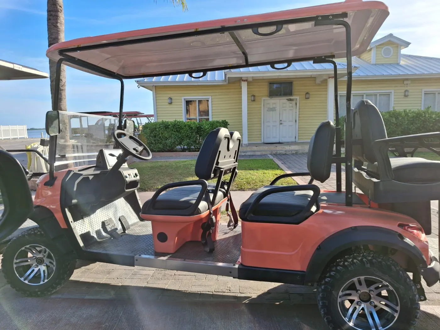 A coral-colored 6-seater golf cart from Utopic Bimini parked in front of a yellow Bahamian-style building